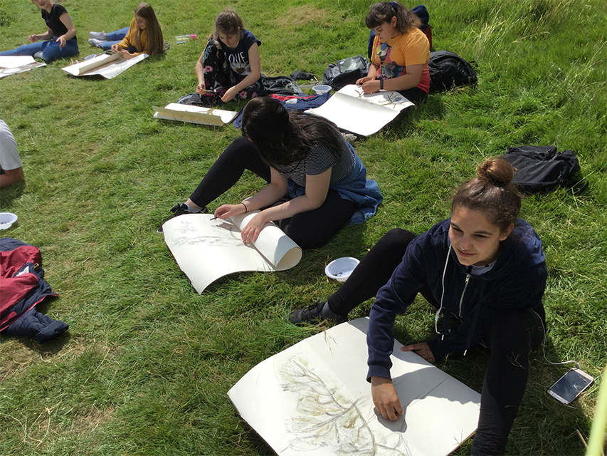Six people in a field drawing the view on paper