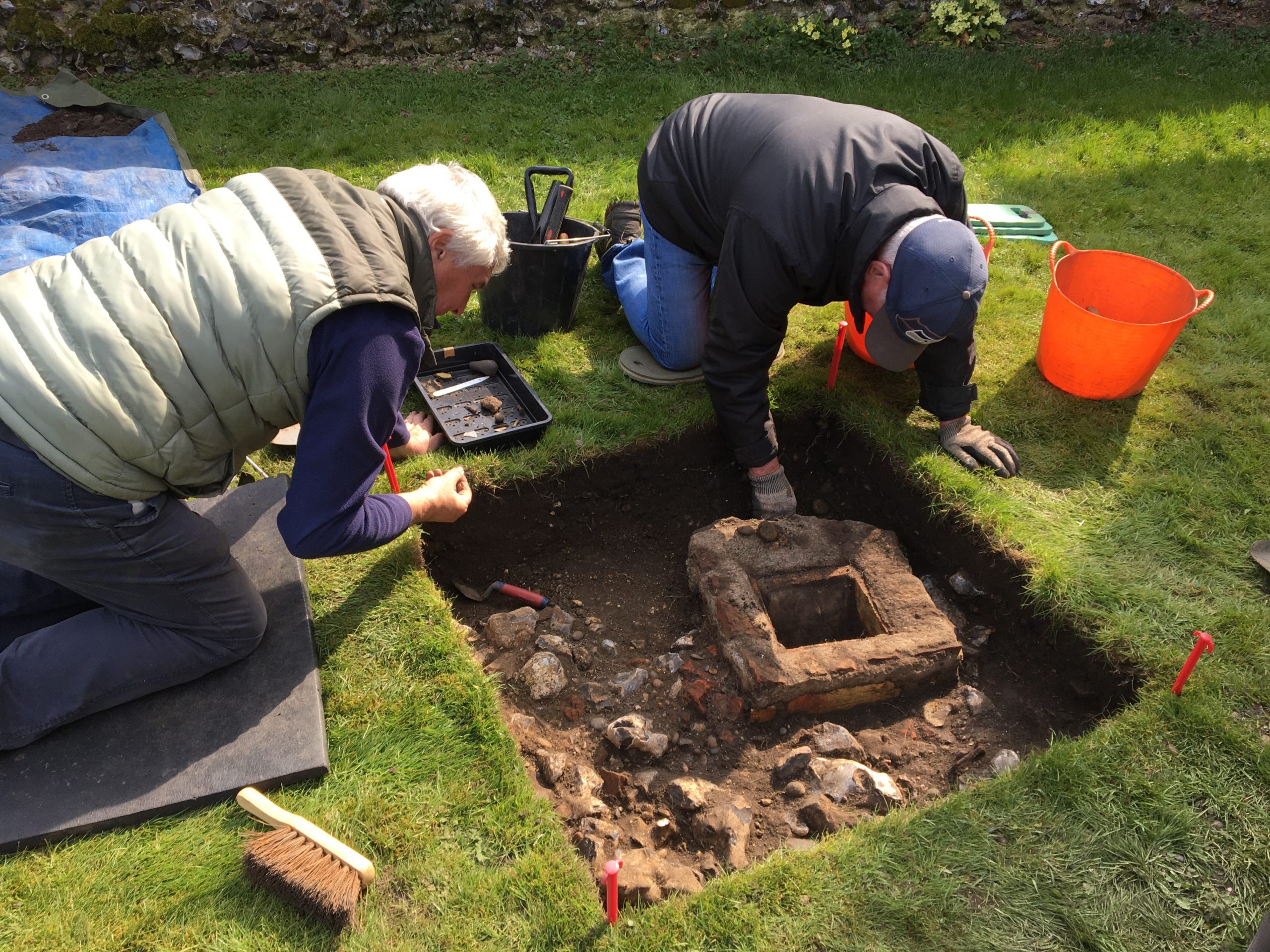 Two men digging a hole in grass with archaeological remains inside