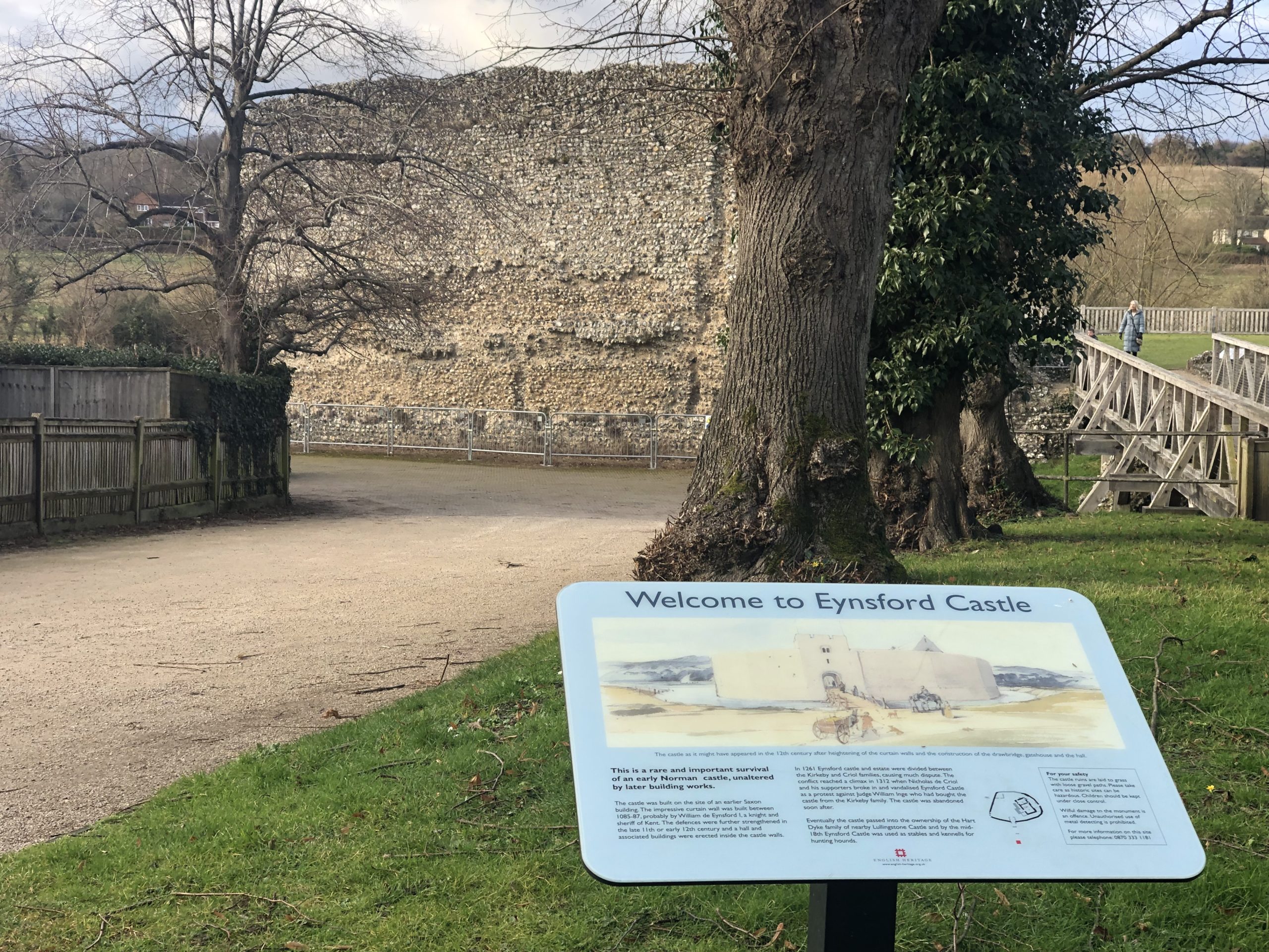 Sign saying welcome to Eynsford Castle with castle wall behind