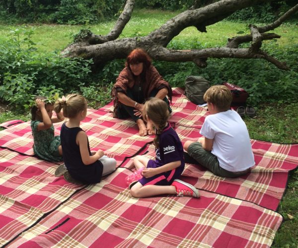 Four children and one adult sat on blanket in woodland