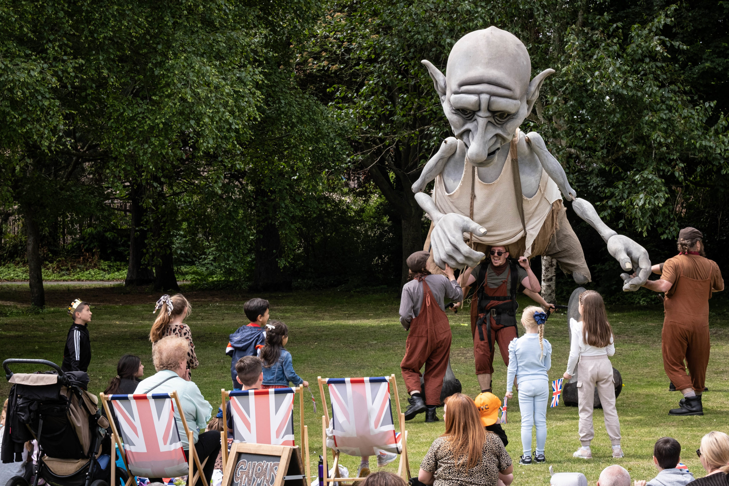 Extra large puppet being moved by three people in front of people sitting on deckchairs