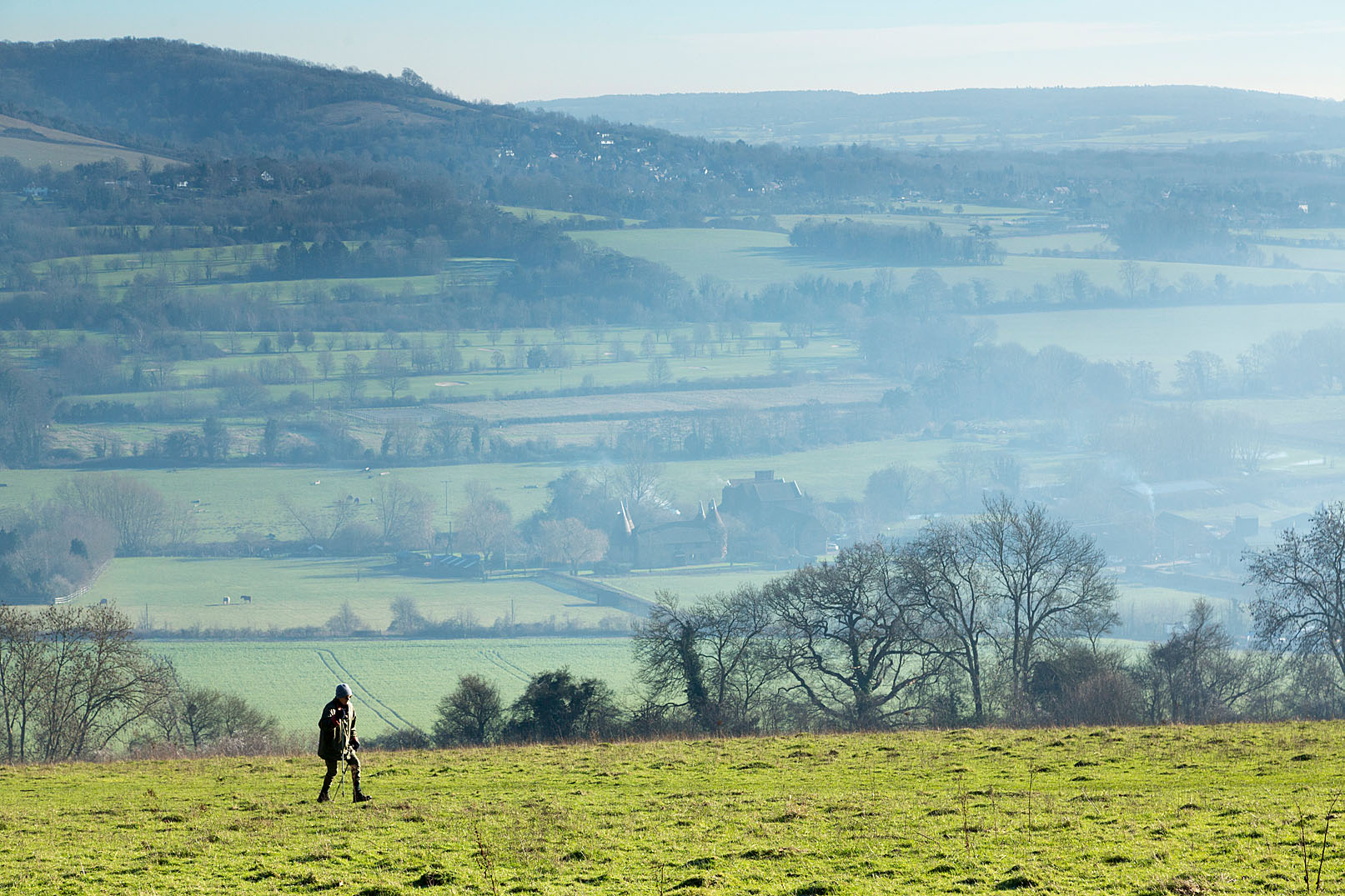 Person walking across green field with panoramic views behind