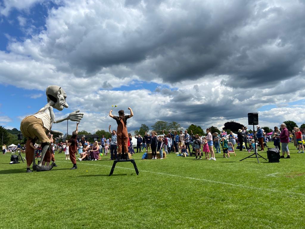 Large puppet with three people moving it in front of a crowd of people on a field